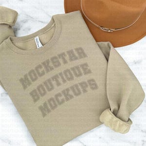 Pu&ograve; includere: Una felpa beige con la scritta "MOCKSTAR BOUTIQUE MOCKUPS" stampata in un font grigio scuro con contorno.