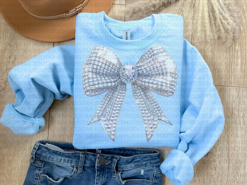 May include: A light blue sweatshirt with a large silver sparkly bow on the front. The bow has a large rhinestone in the center.