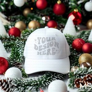 May include: White baseball cap with a white "YOUR DESIGN HERE" text on the front, surrounded by a festive Christmas arrangement of pine branches, red and gold ornaments, and white pinecones.