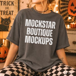 May include: A charcoal gray short-sleeve t-shirt featuring the white distressed text MOCKSTAR BOUTIQUE MOCKUPS printed in a bold, sans-serif font across the chest. The garment has a crew neckline and a relaxed, loose-fitting silhouette.