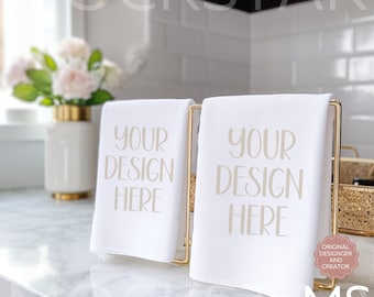 May include: Two white kitchen towels with gold text that reads "Your Design Here" displayed on a gold metal stand. The towels are on a white marble countertop.