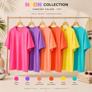 May include: A display of six brightly colored t-shirts hanging on a clothing rack. The shirts are in neon pink, violet, cantaloupe, red orange, lemon yellow, and blue lagoon. The text "NEON COLLECTION" is at the top.