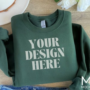Puede incluir: Una sudadera verde oscuro con el texto "YOUR DESIGN HERE" impreso en blanco en la parte delantera.