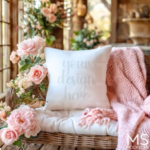 May include: White throw pillow with the text "your design here" on a wicker couch with a pink knitted throw blanket and pink flowers.