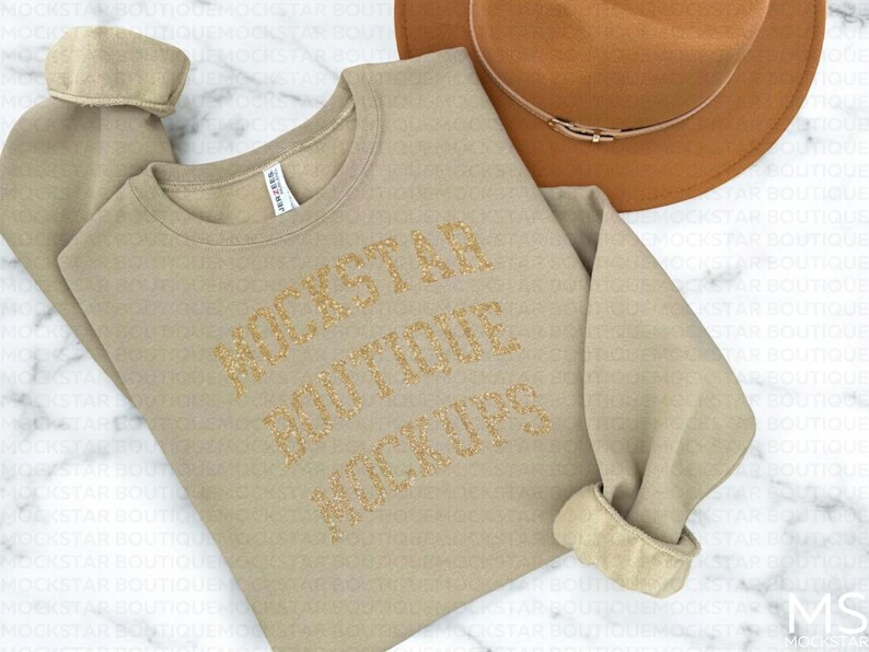 Pu&ograve; includere: Una felpa beige con il testo "Rockstar Boutique Mockups" in lettere di glitter dorate.