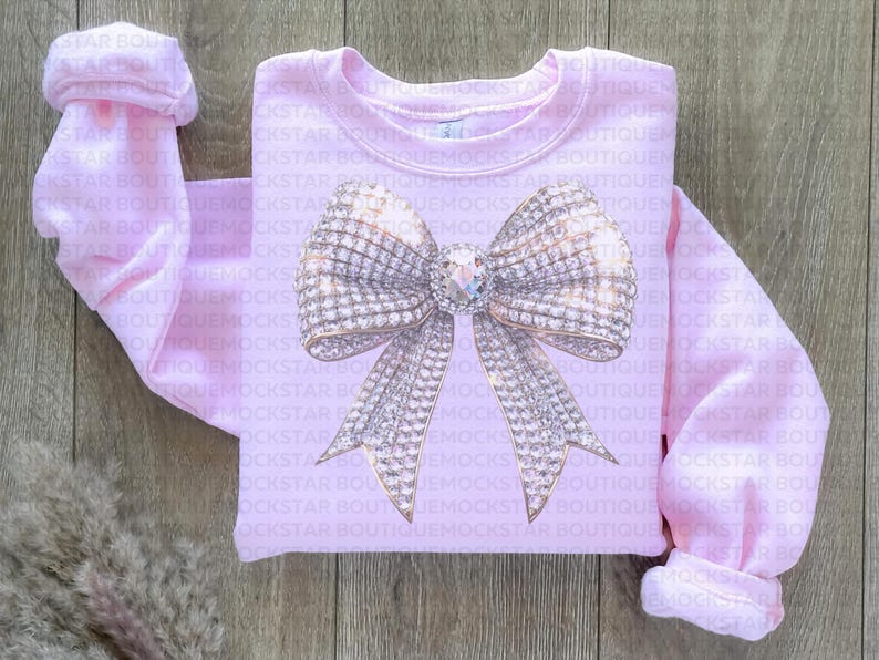 May include: A pink sweatshirt with a large sparkly silver bow design. The bow is made of rhinestones and has a gold center.