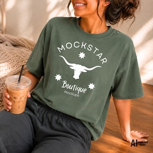 May include: A dark olive green short-sleeve t-shirt featuring a white graphic of a longhorn steer skull centred between three star icons. The text reads MOCKSTAR in an arched font above the skull and Boutique Mockups written below it.