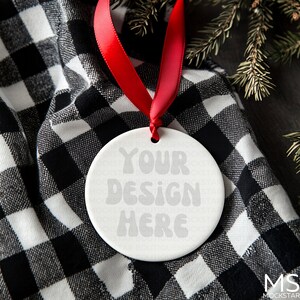 May include: White ceramic ornament with a red ribbon. The ornament has the text "YOUR DESIGN HERE" printed on it.