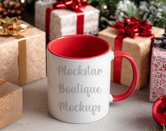 May include: A white ceramic mug with a red interior and handle. The mug has the text "Mockstar Boutique Mockups" in a cursive font. The mug is surrounded by wrapped gifts with red bows and Christmas ornaments.