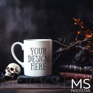 Puede incluir: Una taza de cer&aacute;mica blanca con el texto "YOUR DESIGN HERE" se muestra sobre una superficie de madera. Una peque&ntilde;a calavera y libros antiguos est&aacute;n al lado de la taza. El fondo es oscuro con ramas decorativas.