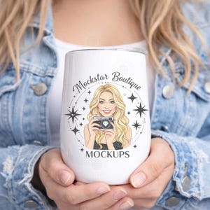 May include: A white insulated tumbler with a black lid, featuring a graphic of a blonde woman holding a camera, surrounded by stars. The text "Mockstar Boutique MOCKUPS" is also on the tumbler.