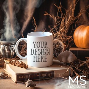 May include: White ceramic mug with the text "YOUR DESIGN HERE" on a brown wooden surface with a book, dried plants, and a pumpkin.