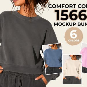 Puede incluir: Un paquete de maquetas Comfort Colors 1566L con una sudadera de cuello redondo gris carbón y pantalones de chándal a juego. El texto dice COMFORT COLORS 1566L MOCKUP BUNDLE 6 COLORS. Las miniaturas adicionales muestran la sudadera en azul, crema y rosa.