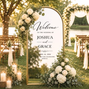 May include: An arched gold-framed mirror wedding welcome sign featuring the text Welcome to the wedding of Joshua and Grace, April 16, 2016, thank you for celebrating with us, decorated with white roses, hydrangeas, and eucalyptus greenery.