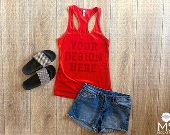 May include: Red tank top with the text "YOUR DESIGN HERE" on a wood background. The tank top is paired with denim shorts and black sandals.