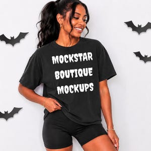 May include: A black short-sleeve t-shirt featuring the white text MOCKSTAR BOUTIQUE MOCKUPS printed in a jagged, distressed font on the chest. The shirt is paired with black fitted shorts, and the surrounding area includes black bat silhouettes.