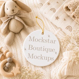 May include: A round white ceramic ornament featuring the text Mockstar Boutique Mockups in a grey serif font, accented by small star icons. The ornament includes a gold hanging string and is displayed alongside a plush rabbit toy and wooden ring.