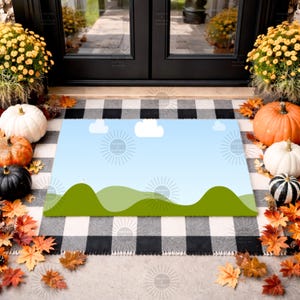 May include: A rectangular doormat with a landscape design featuring green hills, a blue sky, and white clouds. The mat is placed on a black and white checkered rug, surrounded by pumpkins, fall leaves, and yellow flowers.