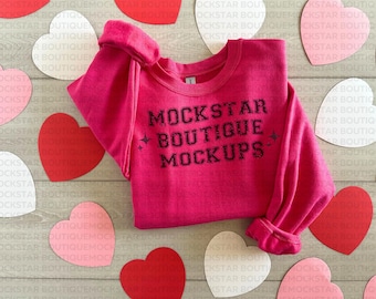Puede incluir: Una sudadera rosa con el texto "MOCKSTAR BOUTIQUE MOCKUPS" impreso en la parte delantera. La sudadera está colocada sobre una superficie de madera con corazones rojos y blancos.