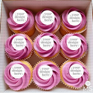 Può includere: Una scatola di nove cupcake con glassa rosa e cerchi bianchi in cima. I cerchi hanno il testo "your design here" su di essi.