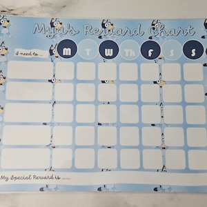 May include: A blue and white reward chart featuring a cartoon dog design. The chart has a grid with spaces for each day of the week. The text "Myia's Reward Chart" is at the top of the chart. The text "I need to..." is at the top left of the chart. The text "My Special Reward is..." is at the bottom left of the chart.