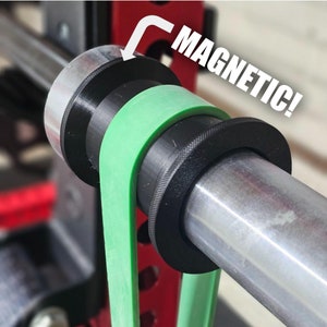 May include: Close-up of a barbell with black magnetic collars and a green resistance band. The word "MAGNETIC!" is written in white text with an arrow pointing to the collar. The barbell is attached to a red weight rack.