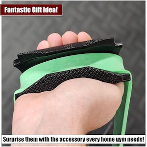 May include: A black and green exercise resistance band with a textured surface. The band is being held in a hand.
