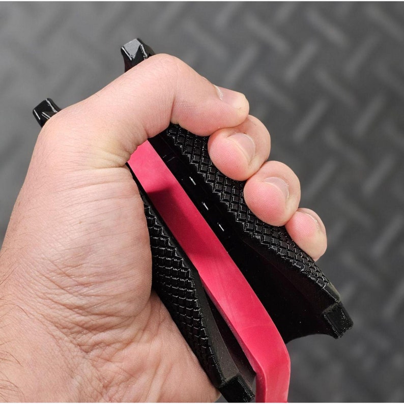 May include: Black and red hand grip with a textured surface. The grip is designed to improve grip strength and forearm development.