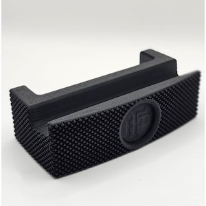 Pode incluir: Porta-cartões de visita de plástico preto com uma superfície texturizada e um logotipo circular. O logotipo é uma letra estilizada "F" dentro de um círculo.