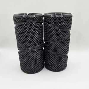 May include: Two black rubber bike grips with a diamond pattern. The grips are designed to provide a secure and comfortable grip.