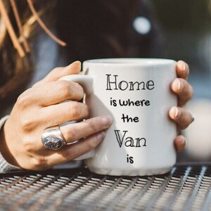 May include: White ceramic mug with black text that reads "Home is where the Van is".