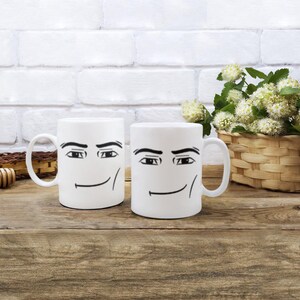 May include: Two white ceramic mugs with black cartoon faces. Each mug has a pair of eyes and a smiling mouth.