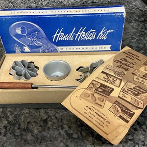 May include: Vintage Handi Hostess kit with waffle and patty shell molds. The blue box reads "Handi Hostess kit" and contains metal molds, a handle, and a booklet. The kit is designed for making tasty entrees and desserts.