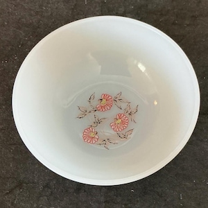 May include: White bowl with a floral design. The bowl has a rounded shape and a smooth surface. The floral pattern features pink flowers with red outlines and brown leaves. The bowl is likely made of ceramic or glass.