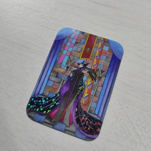K&ouml;nnte beinhalten: Ein Aufkleber mit einer Cartoon-Illustration von Maleficent aus Disneys Dornr&ouml;schen. Sie steht in einem Buntglasfenster mit ihrem Raben und h&auml;lt einen Stab. Der Aufkleber hat ein glitzerndes lila und blaues Design.