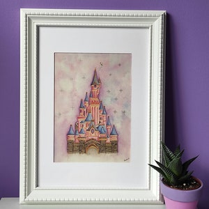 Op de afbeelding: Een ingelijst aquarel schilderij van een roze kasteel met blauwe torens en een witte achtergrond met sterren. Het kasteel is omgeven door een licht roze en blauwe lucht. Het schilderij is in een witte lijst.