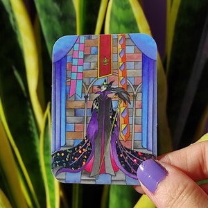 K&ouml;nnte beinhalten: Ein Aufkleber mit einer Cartoon-Illustration von Maleficent aus Disneys Dornr&ouml;schen. Sie tr&auml;gt ein violettes Kleid und h&auml;lt einen Stab. Der Hintergrund ist eine bunte Schlossszene mit Bannern.