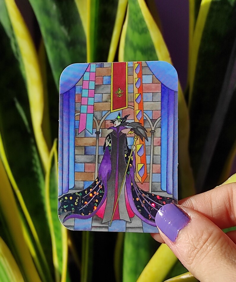 K&ouml;nnte beinhalten: Ein Aufkleber mit einer Cartoon-Illustration von Maleficent aus Disneys Dornr&ouml;schen. Sie tr&auml;gt ein violettes Kleid und h&auml;lt einen Stab. Der Hintergrund ist eine bunte Schlossszene mit Bannern.