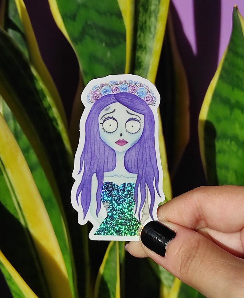 K&ouml;nnte beinhalten: Ein Aufkleber mit einer Comicfigur mit lila Haaren, einer blauen und wei&szlig;en Blumenkrone und einem gr&uuml;n glitzernden Kleid. Die Figur hat einen traurigen Gesichtsausdruck.