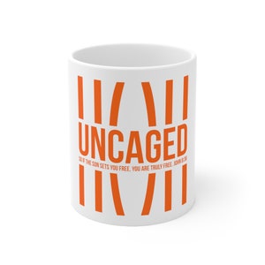 May include: White ceramic mug with an orange design. The design features the word "UNCAGED" with vertical lines and the text "SO IF THE SON SETS YOU FREE, YOU ARE TRULY FREE. JOHN 8:36"