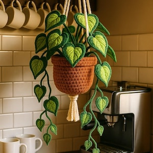 May include: A handmade crochet hanging plant with a brown pot and trailing green and yellow leaves. The plant is suspended by white cords, adding a touch of nature to any space. The plant is a unique, handcrafted item.