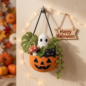 May include: A crocheted orange jack-o'-lantern hanging basket containing a white ghost, a black cat, a red and white mushroom, and green foliage. A wooden sign with the text "Happy Halloween" hangs next to the basket on a string of lights.