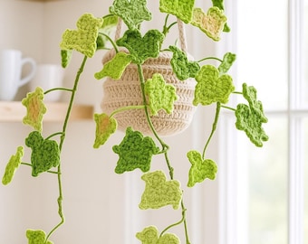 May include: A handmade crochet hanging plant with green ivy leaves. The plant is in a beige crochet pot suspended by a cream-colored rope. The leaves vary in shades of green and yellow.