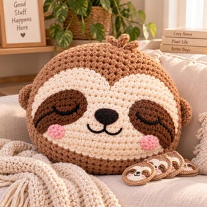 Peut inclure: Un coussin rond au crochet en forme de paresseux avec un visage crème, des taches oculaires marron foncé, un nez noir et des joues roses. Le coussin a un corps marron texturé et est accompagné de quatre petits dessous de verre assortis.