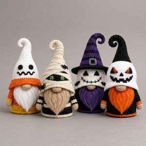Op de afbeelding: Vier gehaakte kabouters met Halloween-thema's. De eerste is een wit spook met een oranje en gele basis. De tweede is een beige mummie met zwarte spinnen. De derde is een paarse heks met een gezicht. De vierde is een zwarte pompoenfiguur.