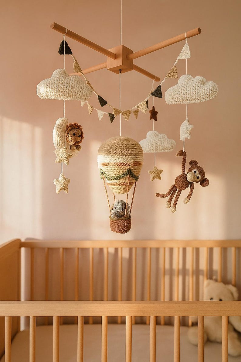 May include: A handmade crochet baby mobile featuring a hot air balloon, clouds, stars, a lion in a crescent moon, and a monkey. The mobile is suspended above a wooden crib, creating a whimsical nursery decor.