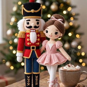 May include: A crocheted nutcracker doll in a red, blue, and black uniform with gold accents, standing beside a crocheted ballerina doll wearing a pink dress and ballet slippers. Both dolls feature detailed yarn hair and embroidered facial features.