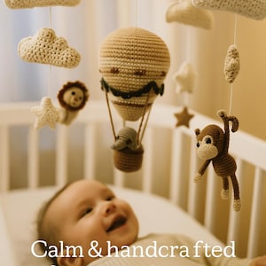 May include: A handmade baby mobile with crochet clouds, stars, a lion, a monkey, and a hot air balloon. The mobile is suspended above a baby in a crib. Text on the image reads "Calm & handcrafted for sweet dreams."