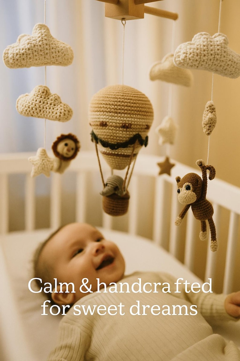 May include: A handmade baby mobile with crochet clouds, stars, a lion, a monkey, and a hot air balloon. The mobile is suspended above a baby in a crib. Text on the image reads "Calm & handcrafted for sweet dreams."