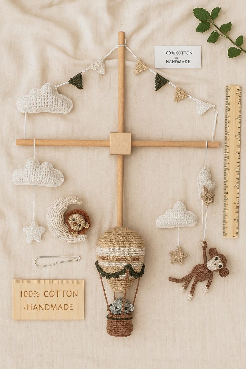 May include: A handmade baby mobile featuring crocheted clouds, stars, a moon with a lion, a hot air balloon with a koala, and a monkey. The mobile is made of beige, brown, and white yarn, with wooden accents. The text "100% Cotton Handmade" is visible.